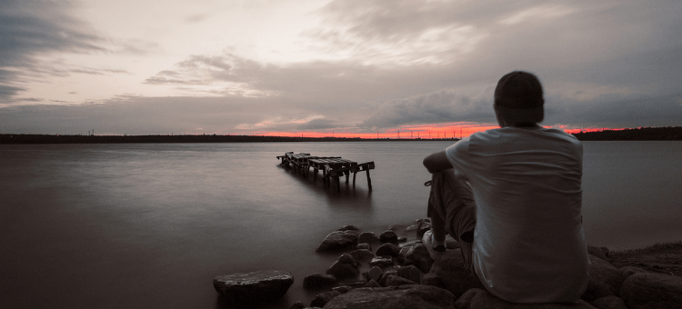 Depression - Mann schaut depressiv über das Meer in den Sonnenuntergang