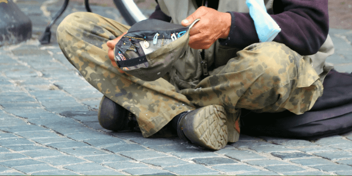 Bettler mit Kappe in der Hand am Boden sitzend