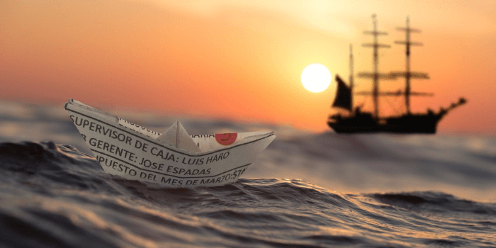 Papierfaltboot vor einem Segelboot auf dem Meer