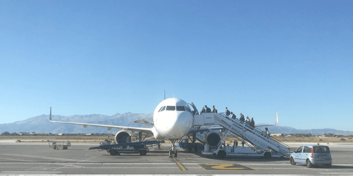 Ein Flugzeug auf dem Rollfeld. Über die Gangway steigen Menschen ein