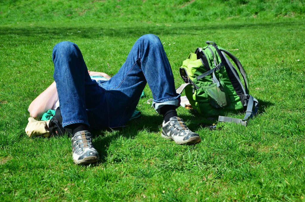 Mann liegt im Gras, neben sich ein Rucksack