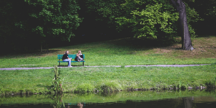 Paar sitzt auf einer Bank vor einem See und spricht miteinander
