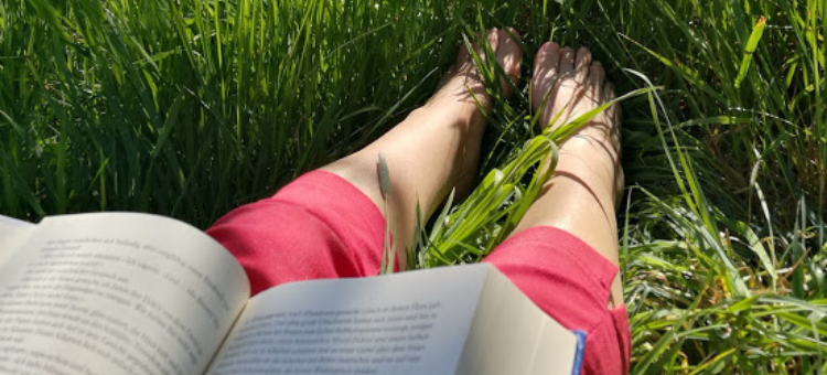 Frau im Gras sitzend und lesend