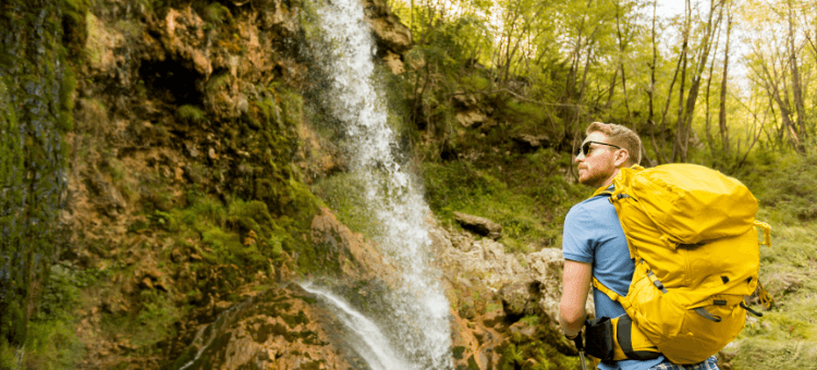 Angst dein Ding zu machen - Mann mit Trekking-Rucksack auf dem Rücken von hinten zu sehen vor einem Wasserfall