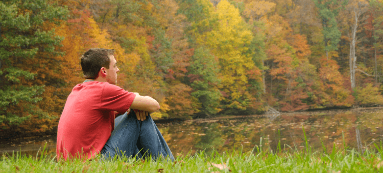 Mann sitzt am See und denkt über den Sinn des Lebens nach
