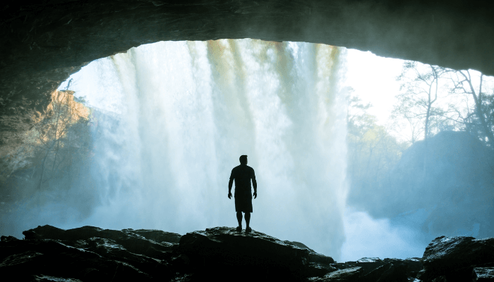 Lektion des Lichtes: Mensch steht auf Klippe hinter einem Wasserfall