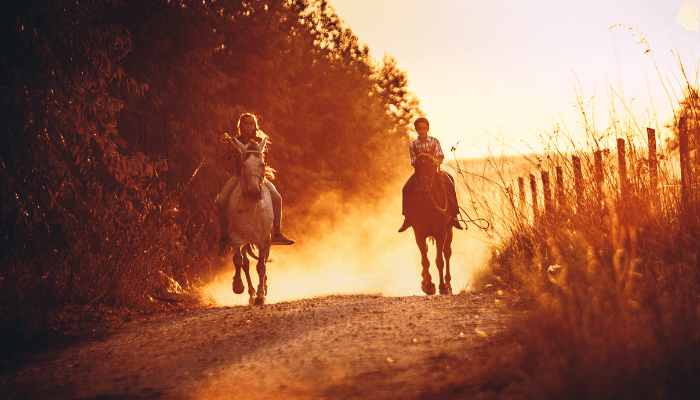 Mädchen und Junge reiten auf einem staubigen Weg entlang.