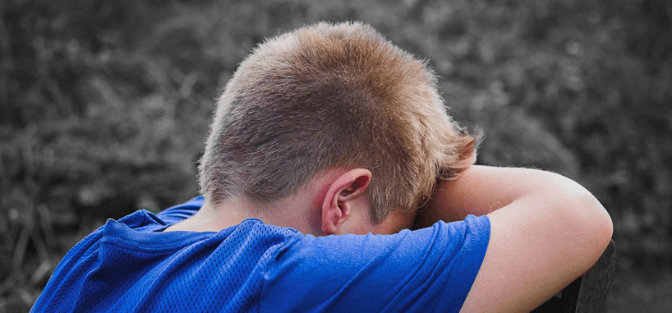 Junge, der weinend den Kopf in die Arme legt