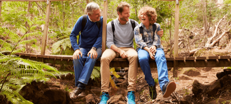 Der Humor des Herzens. Opa, Papa, Sohn auf einer Holzbrücke lachend