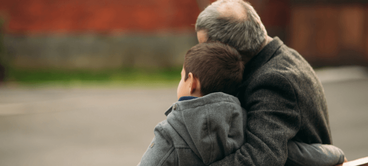 Opa und Enkel sitzen eng umarmend auf einer Bank und stricken die Realität