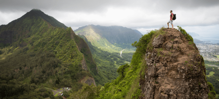 Mann steht auf Berggipfel und schaut ins Tal