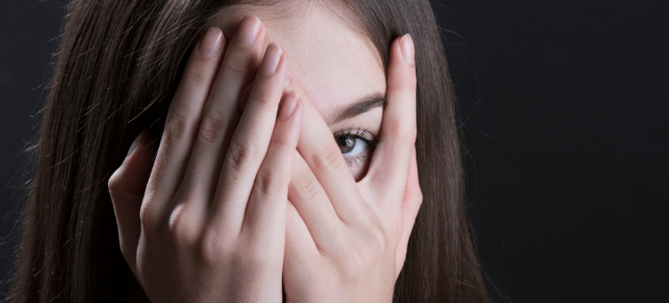 Frau hält beide Hände vor das Gesicht und spreizt fürs linke Auge die Finger