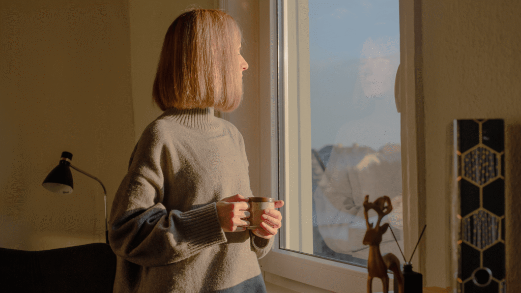 Frau mit Tasse in der Hand schaut aus dem Fenster