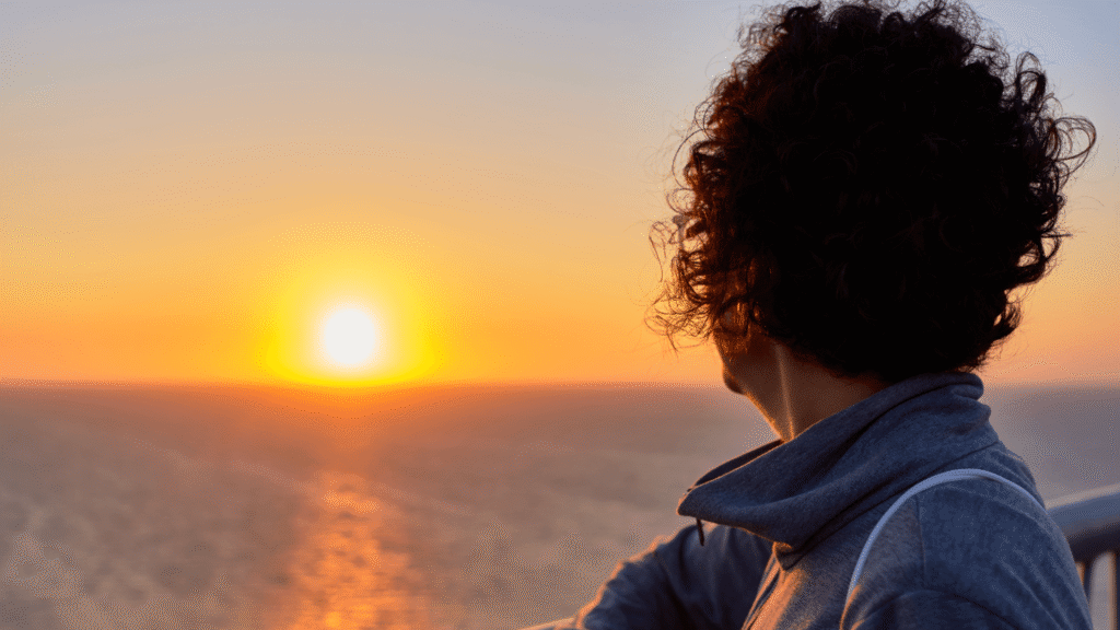Frau schaut übers Meer in einen Sonnenuntergang