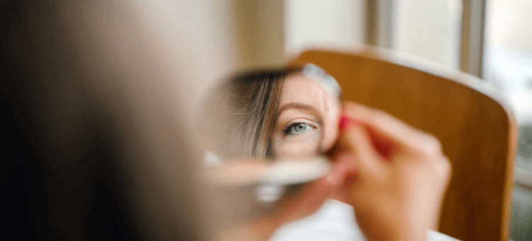 Frau schaut in Spiegel, man sieht ein Auge und Nase